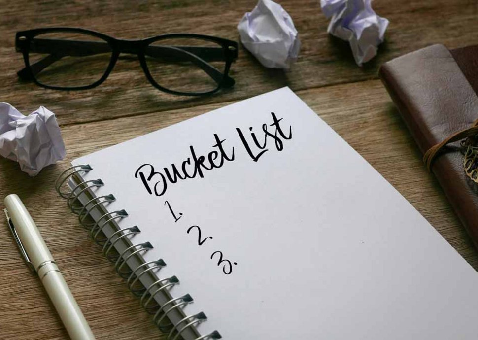 Glasses, balled up paper, pen, and notebook with bucket list written on the page