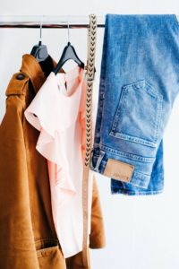 Tan suede jacket, belt, blue jeans, and pink short sleeve top hanging on a clothes rack. Outfit ideas for senior pictures.