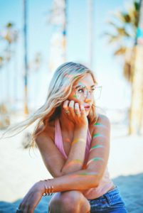 Girl on the beach with glasses, a pink tank top, and blue jean shorts. Best Location for Senior Photos