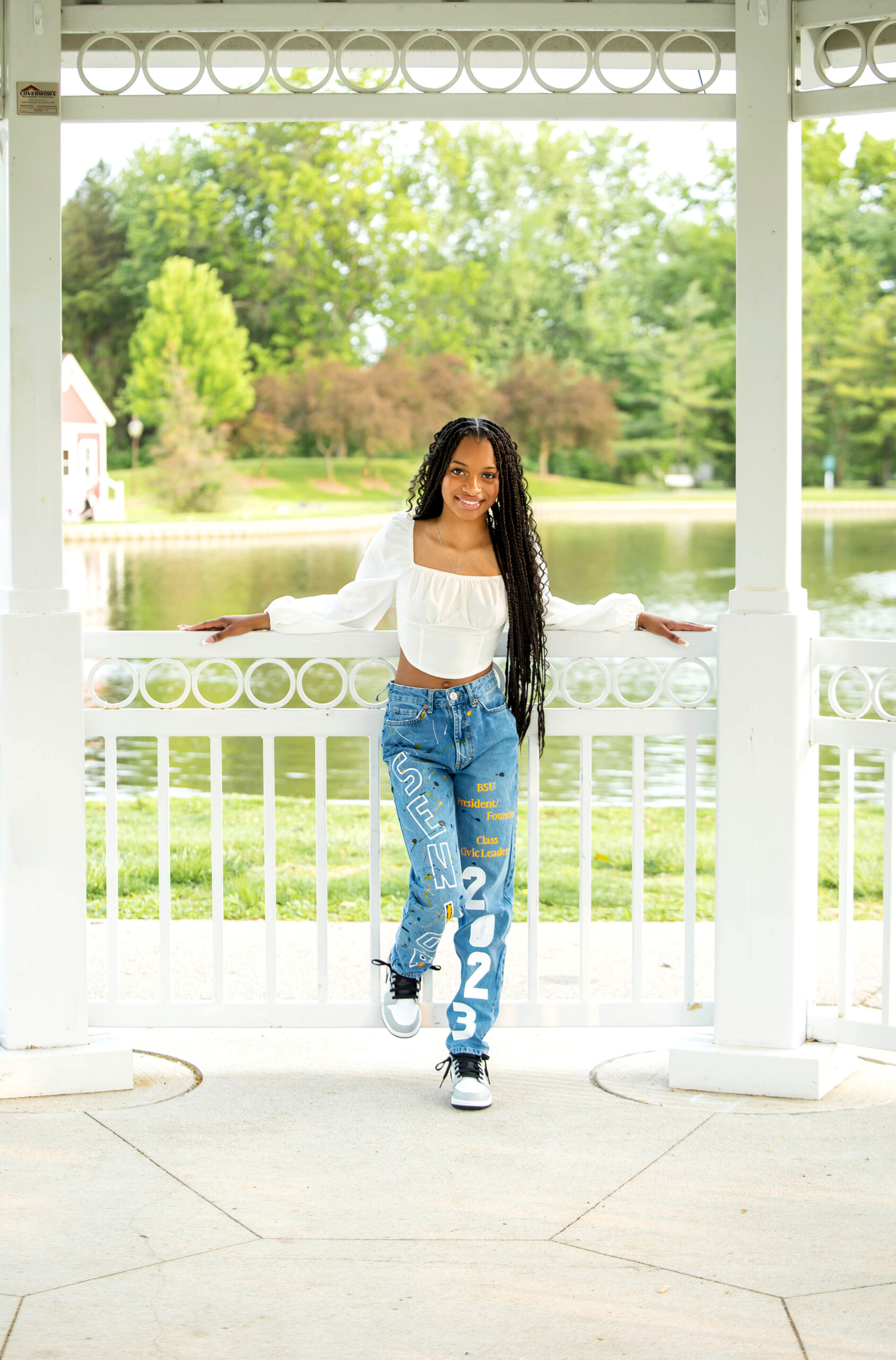 African American girl standing in a gazebo wearing a white blouse and decorated blue jeans in Taylor Heritage Park. Taylor Senior Photographer