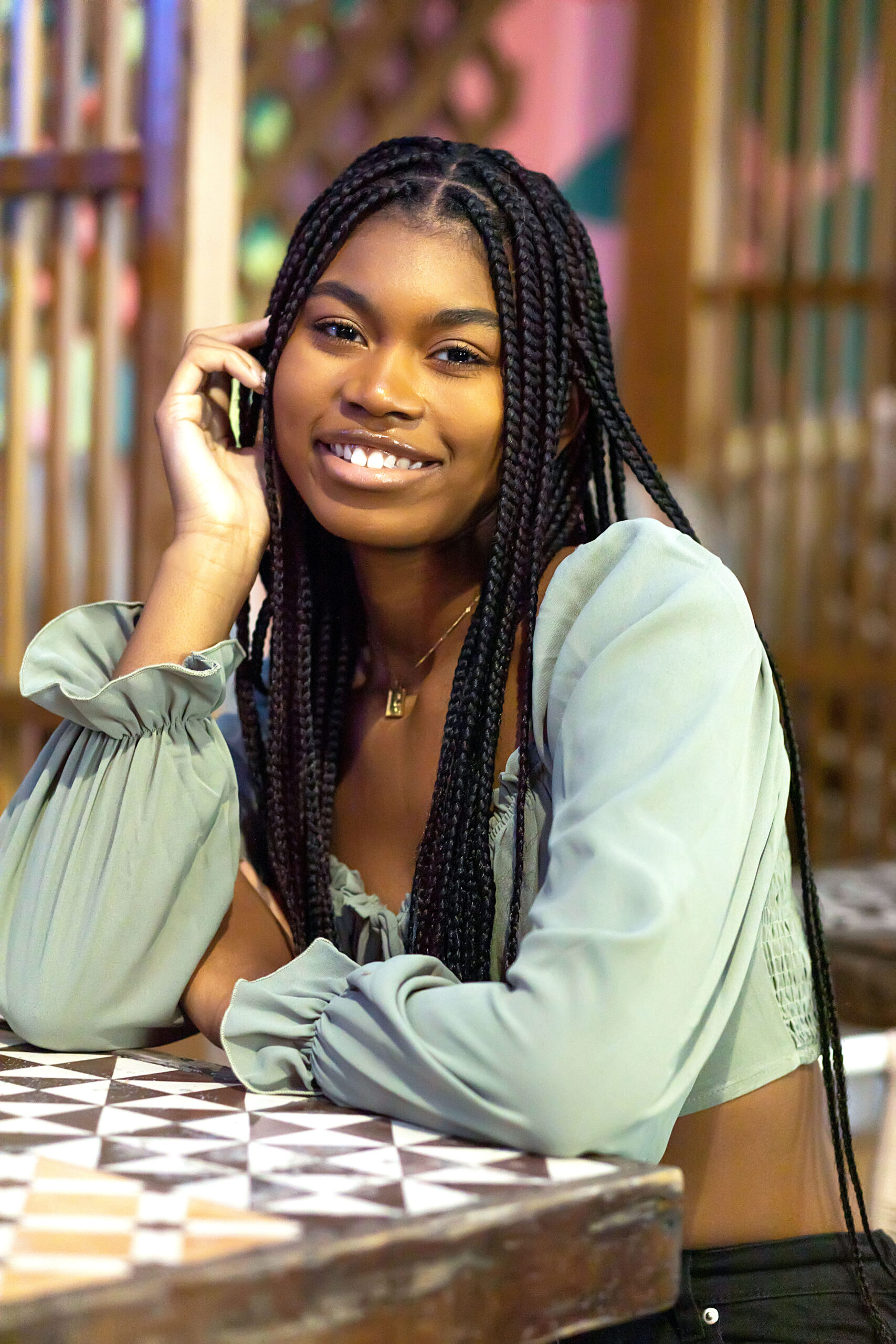 Senior girl with braids wearing sea green long sleeve crop top and black destructed jeans sitting at a table posing casually. Detroit Senior Photogrpher